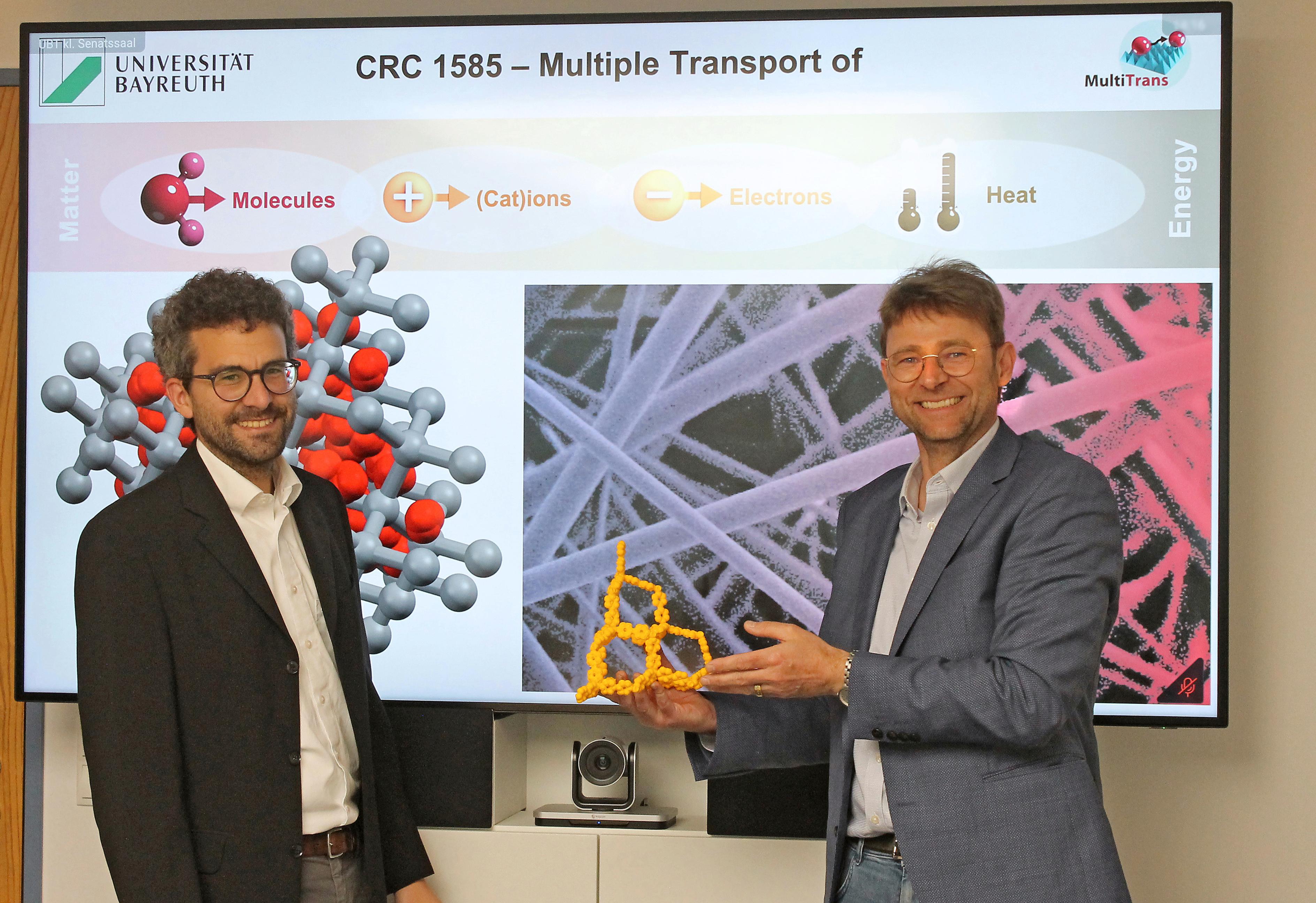 Prof. Dr. Jürgen Senker (re.) und Prof. Dr. Markus Retsch (li), in der Mitte (gelb): 3D-gedrucktes Modell der Porosität von kovalent-organischen Netzwerken.